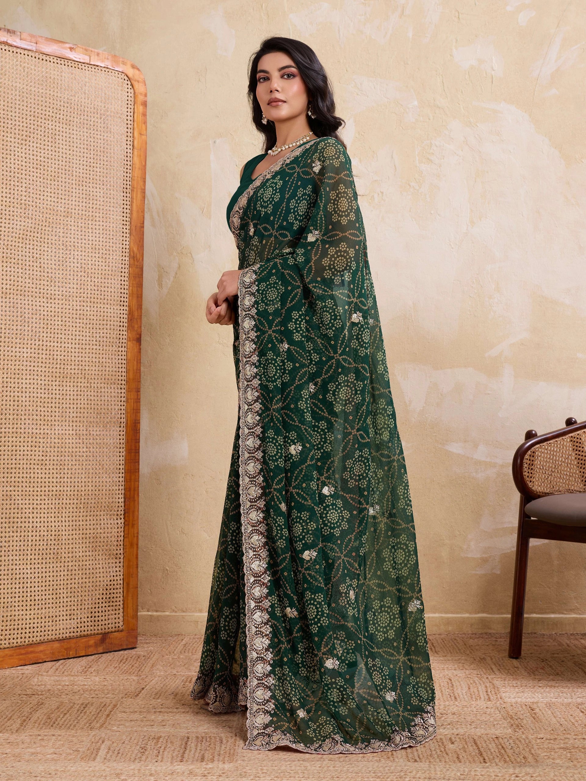 Woman wearing a green embroidered saree in a room with a textured wall and chair.